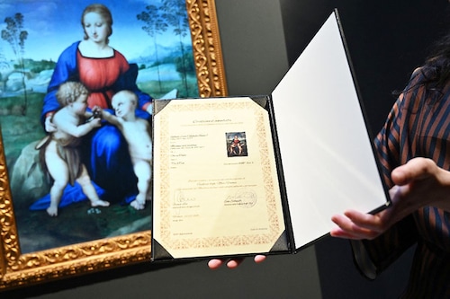 In this file photograph taken on February 15, 2022, a gallery assistant looks at a digital reproduction of the painting "Madonna del Cardellino (Madonna of the Goldfinch" by Raphael, displayed as part of the "Eternalising Art History: From Da Vinci to Modigliani" exhibition at the Unit London gallery in London, where so-called "NFT", (non-fungible token) digital reproductions of six Italian masterpieces, including paintings by Leonardo da Vinci and Amedeo Modigliani, are on display in London as part of the exhibition, entitled "Eternalising Art History". Image: JUSTIN TALLIS / AFP
