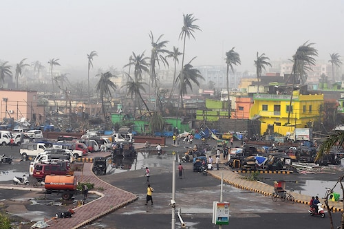 TOPSHOT - People gather next to storm-damaged buildings and palm trees in Puri in the eastern Indian state of Odisha on May 4, 2019, after Cyclone Fani swept through the area. - Cyclone Fani, one of the biggest to hit India in years, barrelled into Bangladesh on May 4 after leaving a trail of deadly destruction in India. (Photo by Dibyangshu SARKAR / AFP) (Photo credit should read DIBYANGSHU SARKAR/AFP/Getty Images)