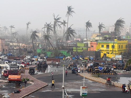 TOPSHOT - People gather next to storm-damaged buildings and palm trees in Puri in the eastern Indian state of Odisha on May 4, 2019, after Cyclone Fani swept through the area. - Cyclone Fani, one of the biggest to hit India in years, barrelled into Bangladesh on May 4 after leaving a trail of deadly destruction in India. (Photo by Dibyangshu SARKAR / AFP)        (Photo credit should read DIBYANGSHU SARKAR/AFP/Getty Images)