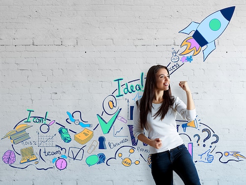 Attractive european woman celebrating success on brick wall background with creative drawn space ship. Successful young entrepreneur
