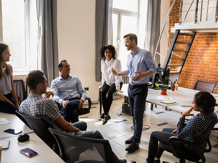 Confident male leader, coach talking with multiracial group of office workers, having good conversation with subordinate, brainstorming, discussing business strategy, ideas, team building activity