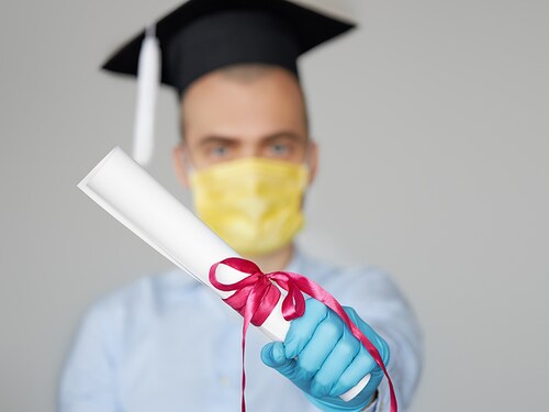 High school graduation during a quarantine. Student graduate in a hat and a protective mask holds a diploma