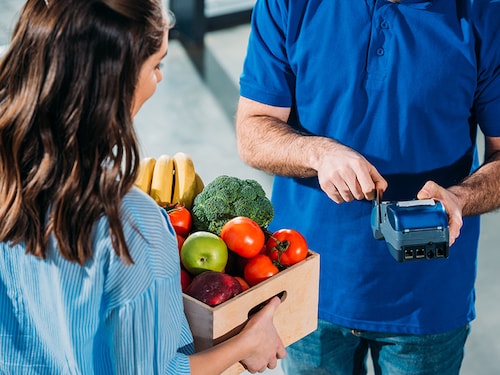 Courier adjusting payment terminal while woman holding groceries in box