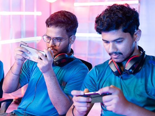 Team of young professional gamers playing live video game on mobile phone by talking on headphones at esports league