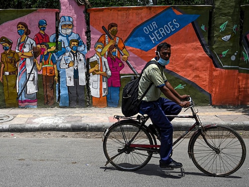 A cyclist passes by a wall mural depicting frontline Covid-19 coronavirus workers, in New Delhi on June 29, 2021. (Photo by Money SHARMA / AFP)