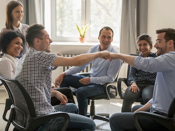 Male colleagues fist bumping at group meeting celebrating good teamwork results concept, happy smiling team office workers sharing success motivated by great relations, corporate culture and support