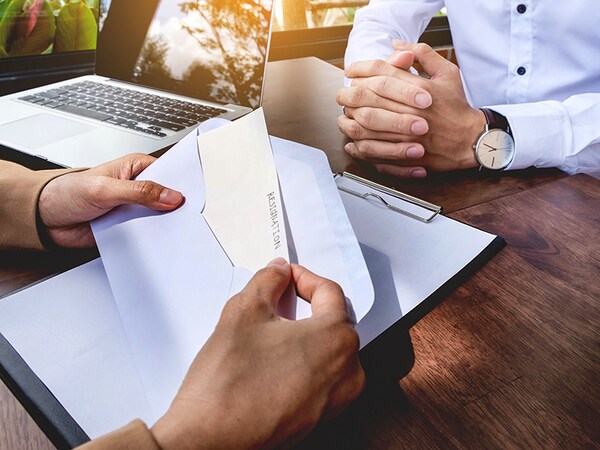 Hand of a businessman hands over a resignation letter on a wooden table to his boss.