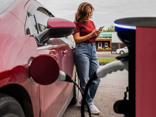 Woman with smartphone next to charging red electric car