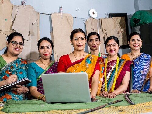 Happy Indian woman using laptop by sewing machine at textile factory
