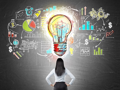 Rear view of businesswoman with hands on waist looking at colorful startup sketch on chalkboard with large light bulb icon in middle. Concept of bright idea.