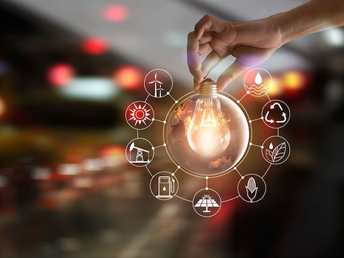 Hand holding light bulb in front of global show the world's consumption with icons energy sources for renewable, sustainable development. Ecology concept. Elements of this image furnished by NASA.