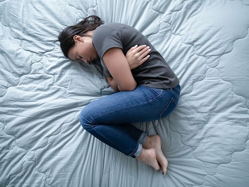 Top view of unhappy depressed young woman lying on bed suffer from abortion or miscarriage, upset female hunch crook in bedroom sleep having emotional breakdown or crisis, healthcare concept