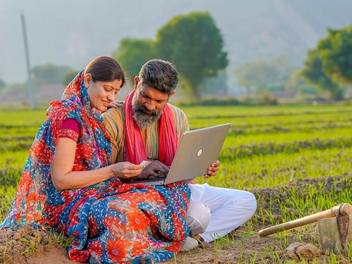 Indian farmer couple use laptop and bank card at agriculture field.