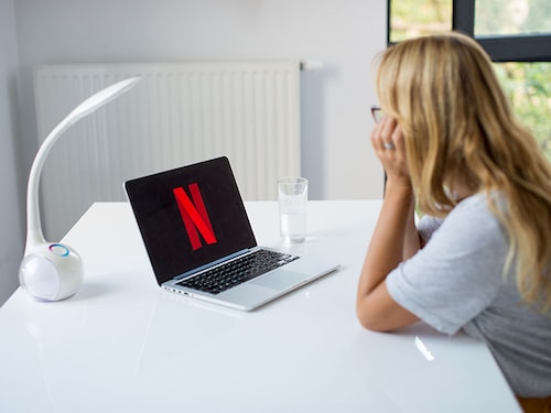 Poznan, Poland, 3.09.2019. Young woman using laptop with Netflix logo in the screen seeting at the office desk. A girl in office watching Netflix.
