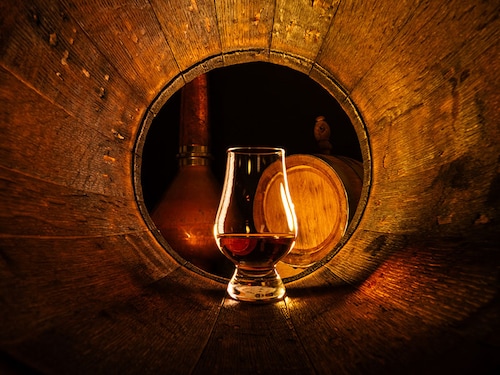 A glass of scotch whiskey in old oak barrel. Copper alambic and small barrel on background. Traditional alcohol distillery concept
