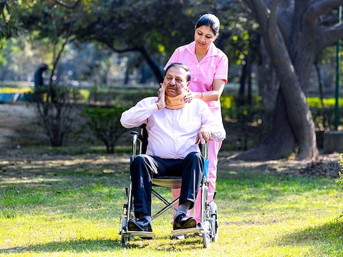 Nurse talking to male senior patient on wheelchair with a neck brace at the park.