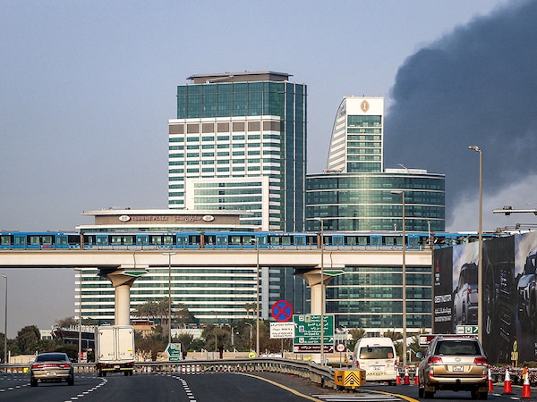 Smoke billows from an ongoing fire near Dubai International Airport as a train of the Dubai Metro moves over vehicles on a highway in Dubai on March 16, 2026. Photo by AFP