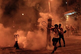 An anti-government activist uses a tennis racket to toss back tear gas bombs at riot police during clashes near the house of the Lebanese Parliament, following Beirut"s massive explosion, which killed at least 158 people, wounded 6000, and displaced some 250,000 to 300,000