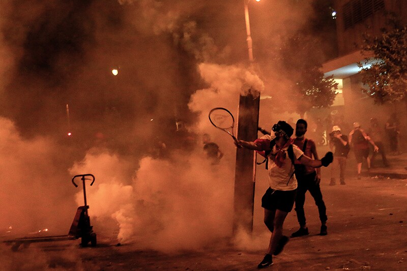 An anti-government activist uses a tennis racket to toss back tear gas bombs at riot police during clashes near the house of the Lebanese Parliament, following Beirut"s massive explosion, which killed at least 158 people, wounded 6000, and displaced some 250,000 to 300,000