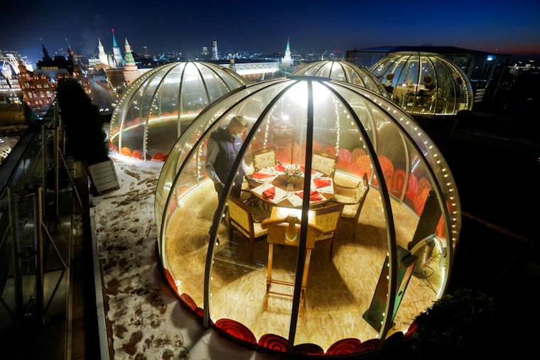 A waiter sets a table inside a transparent pod offered for private Christmas meals with backdrop of the Kremlin and Red Square on the rooftop of Ritz-Carlton hotel in Moscow, Russia December 8, 2020.