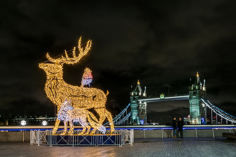 People stand by a reindeer, fox and robin Christmas light installation near London City Hall with Tower Bridge in the background on December 23, 2020 in London, England. Many Christmas events have been cancelled this year due to the coronavirus (COVID-19) pandemic but London is festooned with Christmas lights across the capital.
