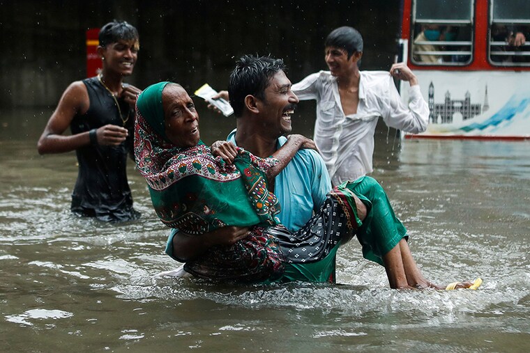 A man carries an elderly woman as they cross a waterlogged street during heavy rainfall in Mumbai, India, July 15, 2020.