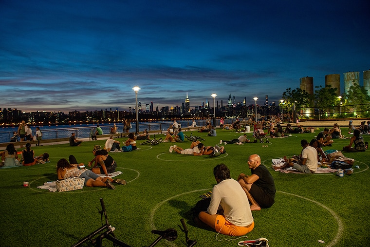 People with and without masks sit in circles to observe social distancing with the Manhattan skyline in the background in Domino Park as the city continues Phase 4 of re-opening following restrictions imposed to slow the spread of coronavirus on July 26, 2020 in New York City. The fourth phase allows outdoor arts and entertainment, sporting events without fans and media production.