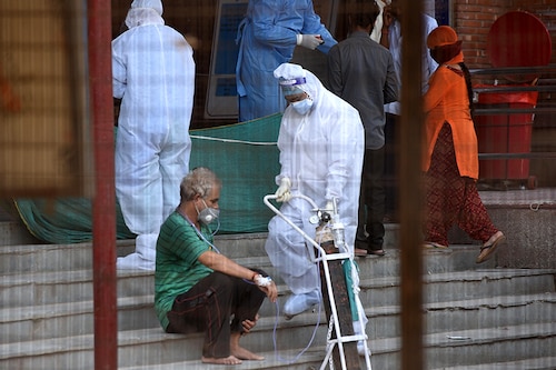 A medical worker in PPE coveralls helps move an oxygen tank being used by a person with breathing issues outside the Covid-19 ward, at Lok Nayak Jai Prakash Narayan Hospital (LNJP) on June 10, 2020 in New Delhi, India.