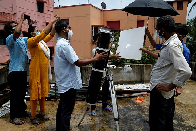 People, wearing protective face masks against the coronavirus disease (COVID-19), use a telescope to cast a reflection of a partial solar eclipse on a board on a rooftop in Kolkata, India, June 21, 2020