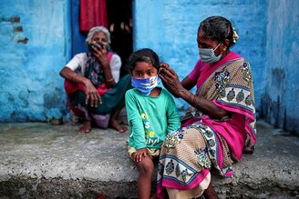 A woman wearing a protective face mask adjusts her daughter"s face mask outside their house at a slum area, during an extended nationwide lockdown to slow the spreading of the coronavirus disease (COVID-19), in New Delhi, India, June 24, 2020.