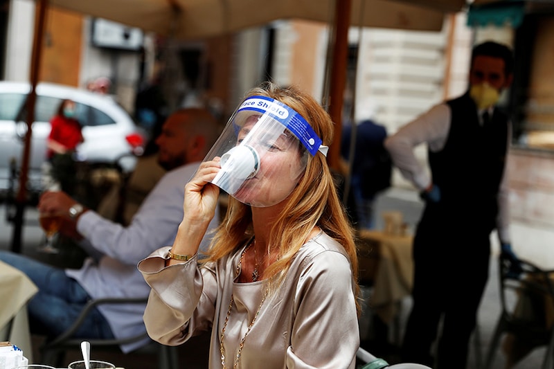 A woman wearing a face shield drinks coffee at a cafe as Italy eases some of the lockdown measures put in place during the coronavirus disease (COVID-19) outbreak, in Rome, Italy.