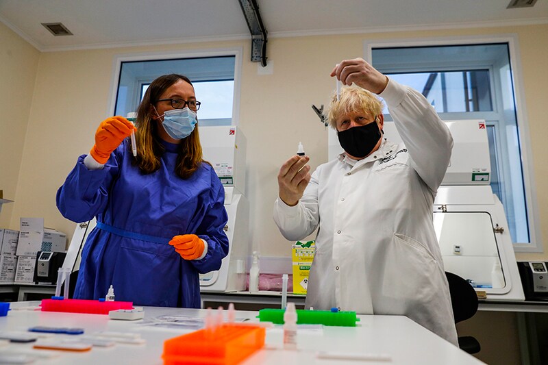 Britain"s Prime Minister Boris Johnson (R) looks at samples at the Lateral Flow Testing Laboratory with Doctor Abbie Bown (L) during a visit to the Public Health England site at Porton Down science park on November 27, 2020. The Public Health England lab in Porton Down is working on a UK-made lateral coronavirus test, which aims to provide test results within minutes. The Prime Minister visited the lab a day after the new coronavirus tier system was announced. The new approach, which puts the vast majority of the population under tight restrictions, has faced backlash from many Conservative MPs who consider it to be too severe.