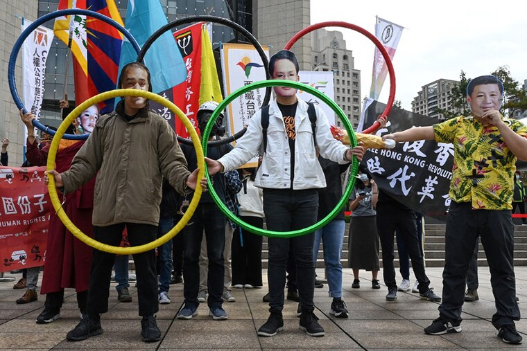 A man (R) wearing a face mask with the image of China"s President Xi Jinping joins other human rights activists holding Olympic Rings as they protest in Taipei against the 2022 Beijing Winter Olympic Games to mark Human Rights Day on December 10, 2021.