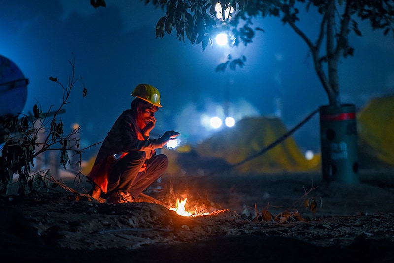 A worker warm himself around a bonfire on a cold winter evening at India Gate, on December 19, 2021 in New Delhi, India.
