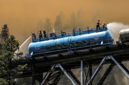 Firefighters spray water from a fire train to hot spots along the tracks over Rock Creek Bridge as the Dixie Fire grows in Plumas National Forest, California, U.S., July 15, 2021.