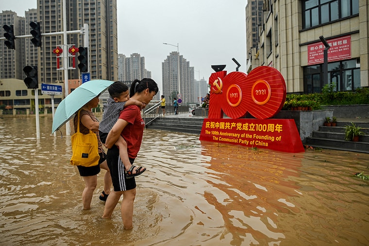 People wade across a flooded street following heavy rains which caused flooding and claimed the lives of at least 33 people earlier in the week, in the city of Zhengzhou in China"s Henan province on July 23, 2021.