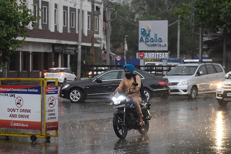 Commuters make their way along a street during a shower of rain in Amritsar, Punjab, on May 31, 2021