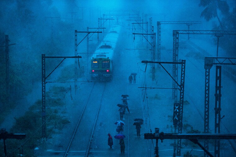 Commuters walk on the railway tracks as local trains are stranded due to waterlogging near Tilak Nagar station on June 9, 2021, in Mumbai, India. The south-west monsoon arrived in Mumbai on Wednesday, the IMD announced, and heavy rains lashed the country"s financial capital and suburbs since early morning. Waterlogging was reported in some low-lying areas, but local train services remained largely unaffected, while routes of some BEST buses were diverted.