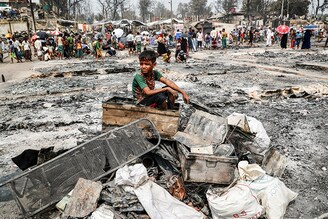 A Rohingya refugee boy sits on a stack of burned material after a massive fire broke out and destroyed thousands of shelters in a Rohingya refugee camp in Cox"s Bazar, Bangladesh, March 24, 2021.