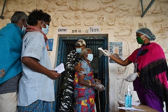 A paramilitary personnel assists an elderly woman while a volunteer checks her body temperature before entering a polling station to cast her ballot during Phase 1 of West Bengal"s legislative election in Purulia district on March 27, 2021.