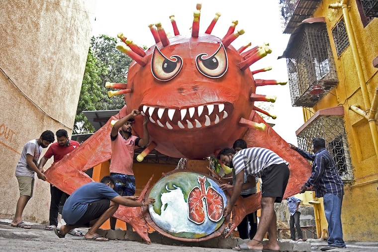 People are seen near a giant effigy resembling the Covid-19 coronavirus to be burned as a part of Holika Dahan, or burning of Indian mythical demon Holika usually performed on the eve of Holi celebrations which is a popular Hindu spring festival of colours in Mumbai on March 28, 2021.
