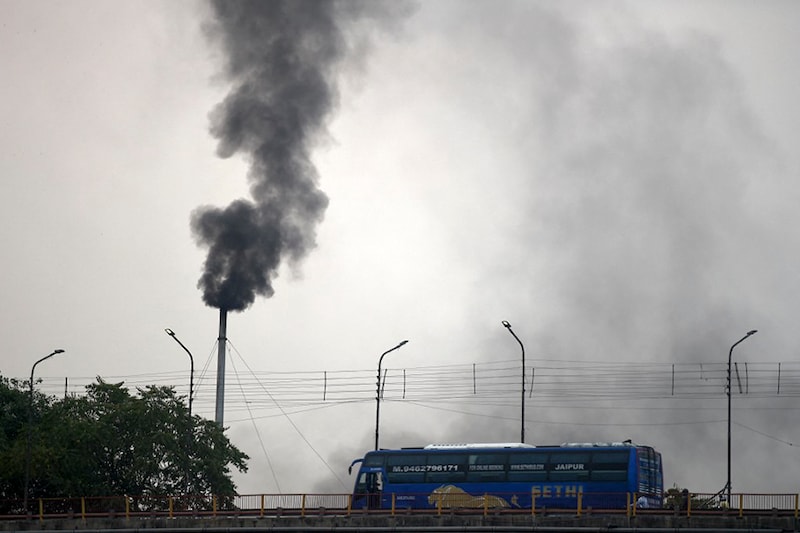 A bus drives along a road as smoke billows from a chimney of a municipal crematorium in Allahabad on May 2, 2021 amidst rising deaths due to the Covid-19 coronavirus.