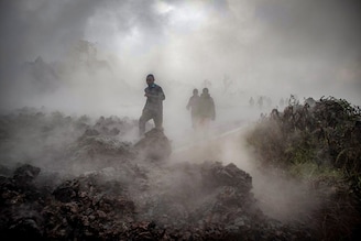 Men cross the front of the still-smoking lava rocks from an eruption of Mount Nyiragongo on May 23, 2021, in Goma in the East of the Democratic Republic of Congo. A river of boiling lava came to a halt on the outskirts of Goma Sunday, sparing the city in eastern DR Congo from disaster after the nighttime eruption of Mount Nyiragongo sent thousands of terrified residents fleeing in panic.