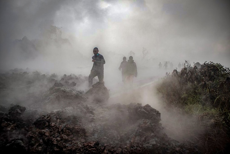 Men cross the front of the still-smoking lava rocks from an eruption of Mount Nyiragongo on May 23, 2021, in Goma in the East of the Democratic Republic of Congo. A river of boiling lava came to a halt on the outskirts of Goma Sunday, sparing the city in eastern DR Congo from disaster after the nighttime eruption of Mount Nyiragongo sent thousands of terrified residents fleeing in panic.