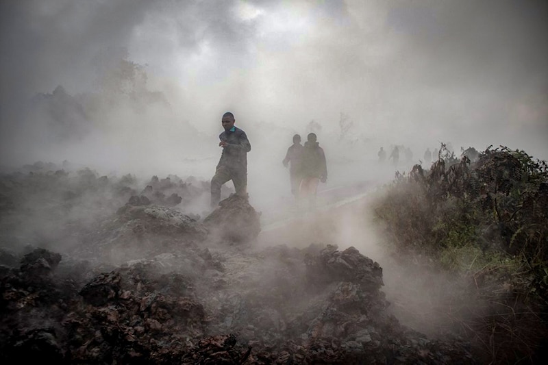 Men cross the front of the still-smoking lava rocks from an eruption of Mount Nyiragongo on May 23, 2021, in Goma in the East of the Democratic Republic of Congo. A river of boiling lava came to a halt on the outskirts of Goma Sunday, sparing the city in eastern DR Congo from disaster after the nighttime eruption of Mount Nyiragongo sent thousands of terrified residents fleeing in panic.