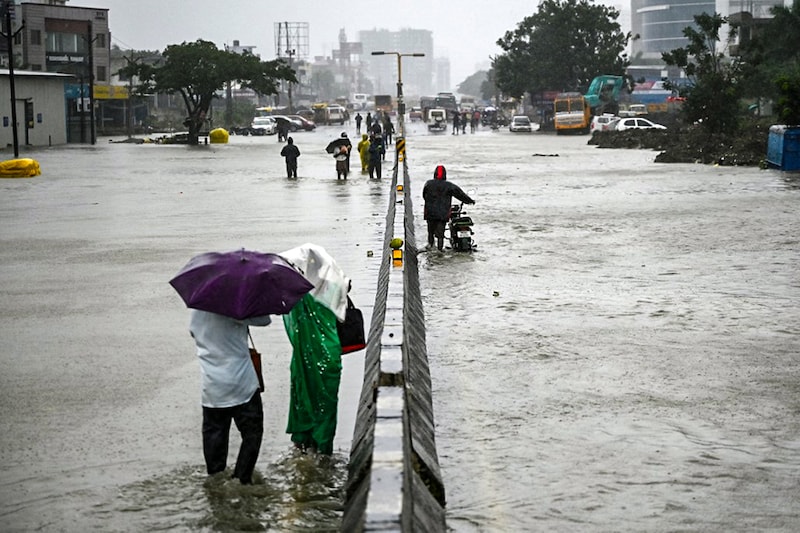 People wade along a waterlogged road during a heavy monsoon rainfall in Chennai on November 11, 2021.