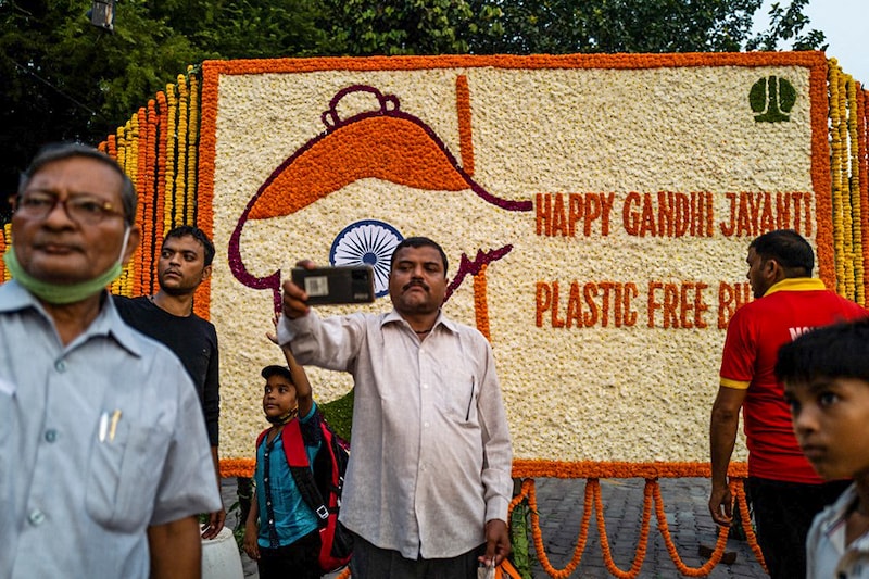 People take selfies in front of a floral arrangement on the eve of ‘Gandhi Jayanti’ marking the birth anniversary of India’s father of the nation Mahatma Gandhi beside a street in New Delhi on October 1, 2021.