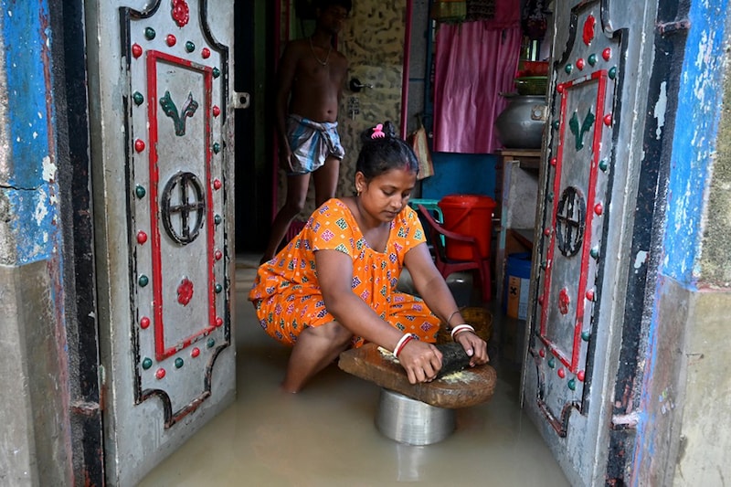 A flood-affected villager prepares spices for cooking inside her flooded house in Howrah district of India’s West Bengal state on October 2, 2021.