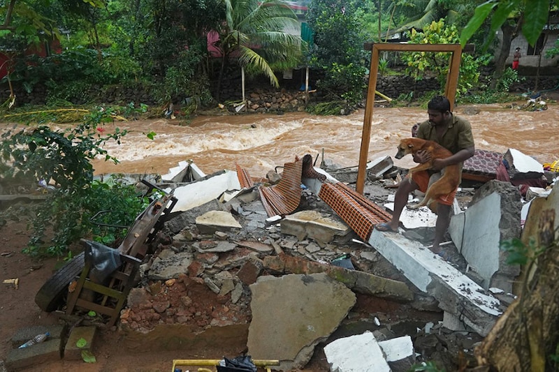 A resident carries a dog amid the debris of his damaged house after flash floods caused by heavy rains in Thodupuzha, Kerala.