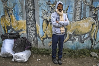 An Indian migrant worker awaits by a wall mural in Srinagar, Kashmir, to board a bus to return to his native home state, on October 19, 2021. Hundreds of labourers who are in Kashmir on work started fleeing the region following attacks on migrant labourers by suspected militants since early this week.